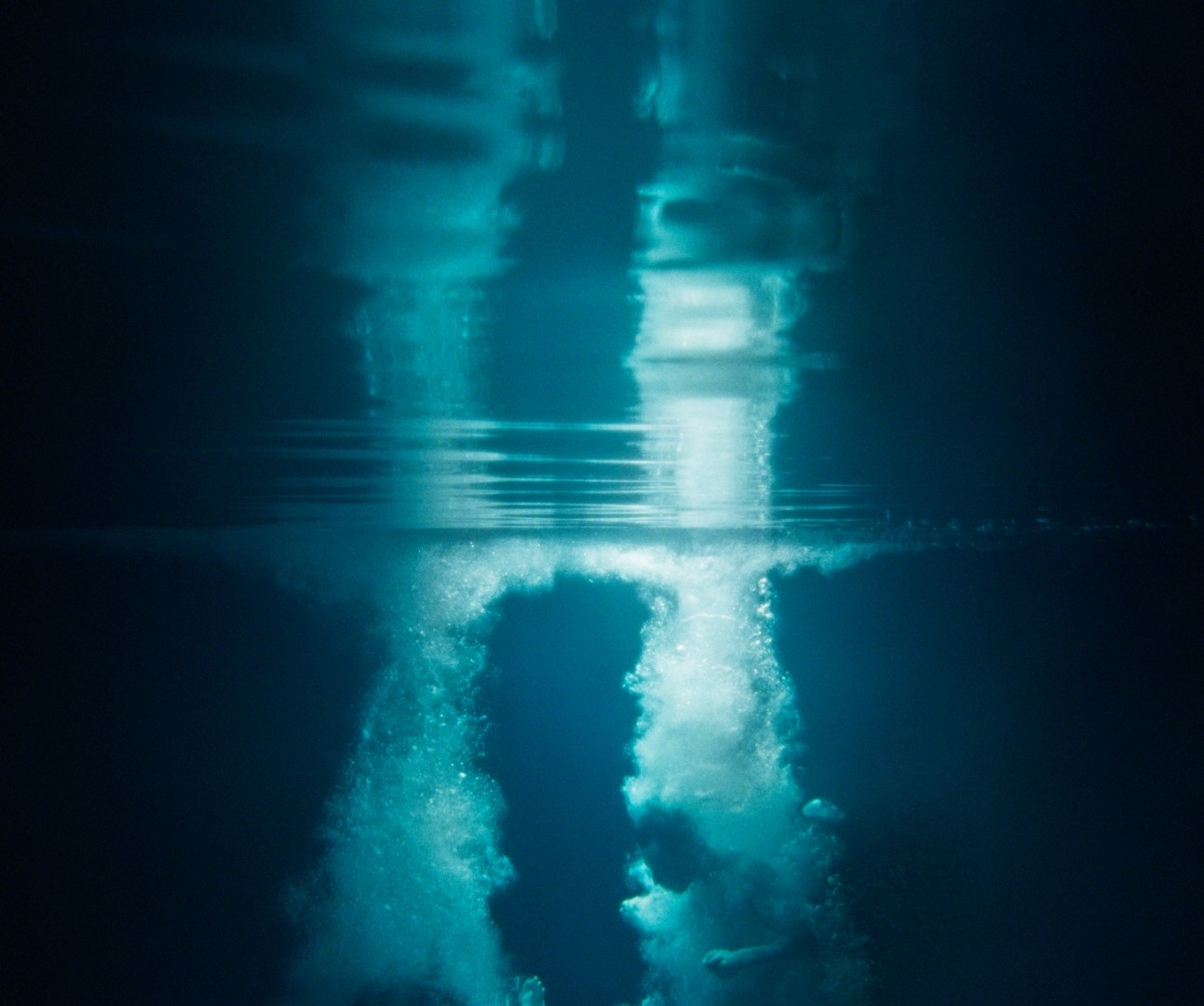 Two figures plunging beneath the surface of dark blue water, trailing columns of bubbles.