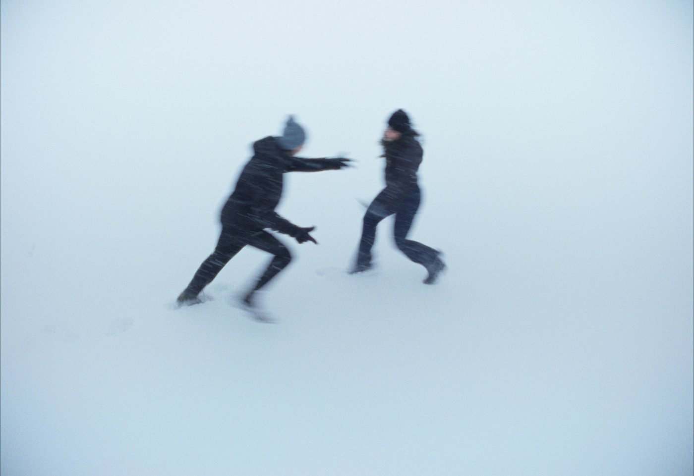 Two figures reaching toward each other in a whiteout of snow.