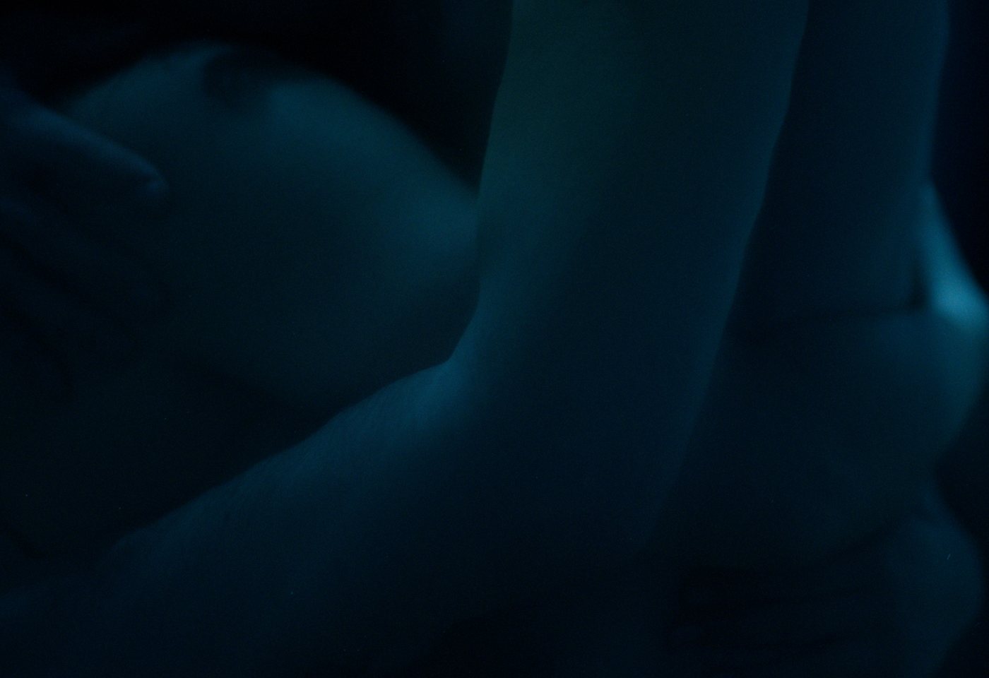 Yasmin and Joseph holding each other in low blue light.